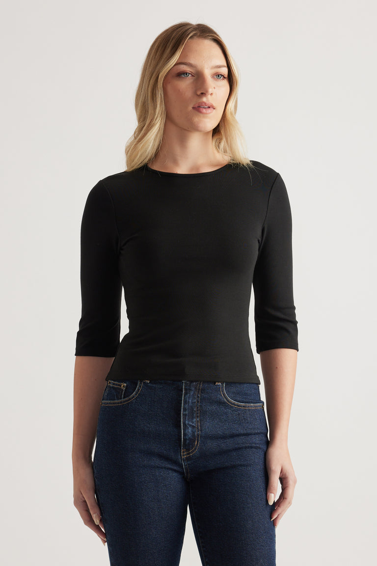Woman wearing a fitted black crew neck top with three-quarter sleeves and dark jeans