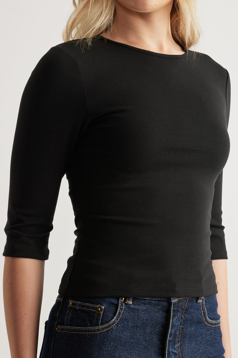 Woman wearing a fitted black crew neck top with three-quarter sleeves and blue jeans
