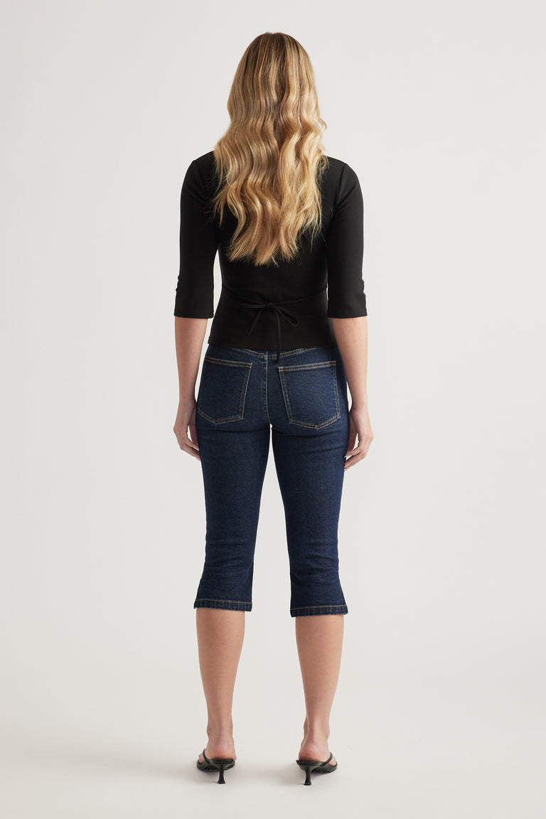 Woman wearing a fitted black three quarter sleeve top with back waist tie and dark cropped jeans