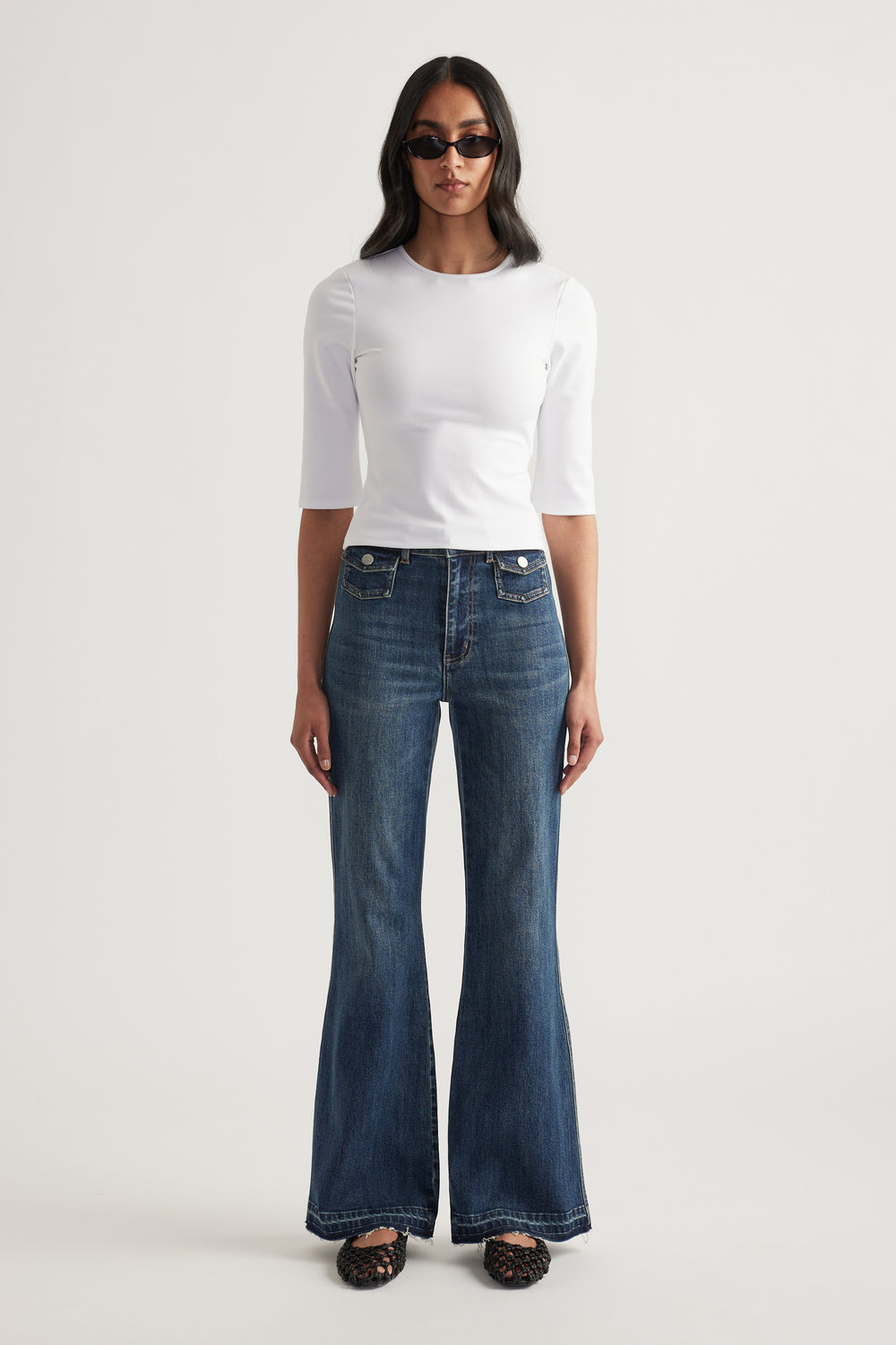 Woman wearing a fitted white three-quarter sleeve top with dark wide-leg jeans and sunglasses