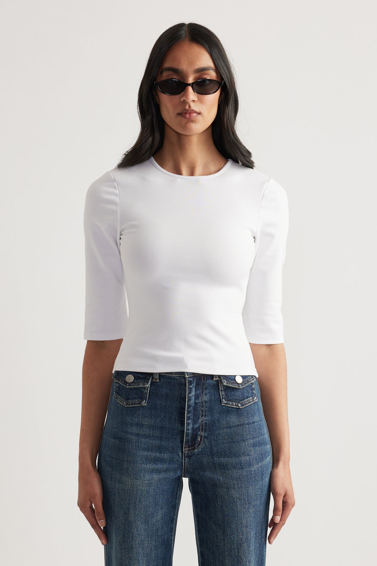 Woman wearing a fitted white three quarter sleeve top with blue jeans and sunglasses