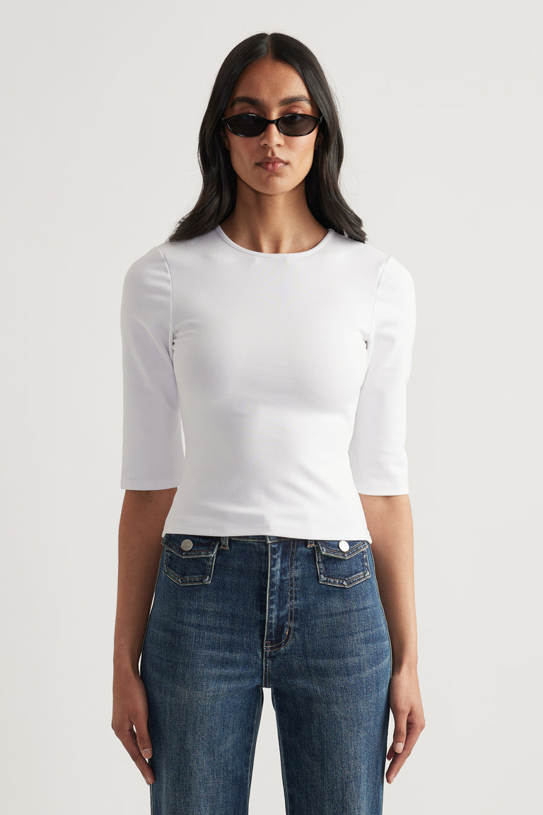 Woman wearing a fitted white three quarter sleeve top with blue jeans and sunglasses