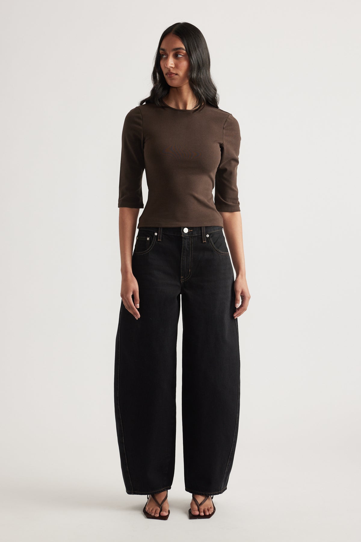 Woman wearing a fitted brown three quarter sleeve top with black wide leg jeans and sandals