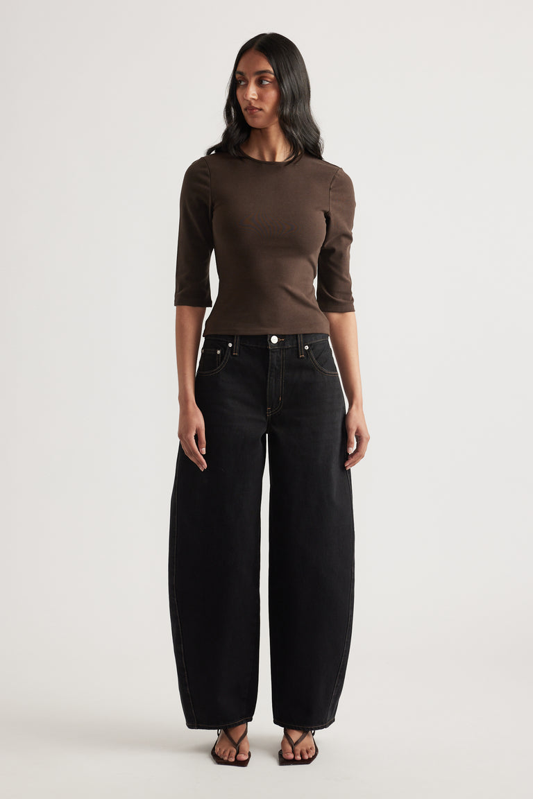 Woman wearing a fitted brown three quarter sleeve top with black wide leg jeans and sandals