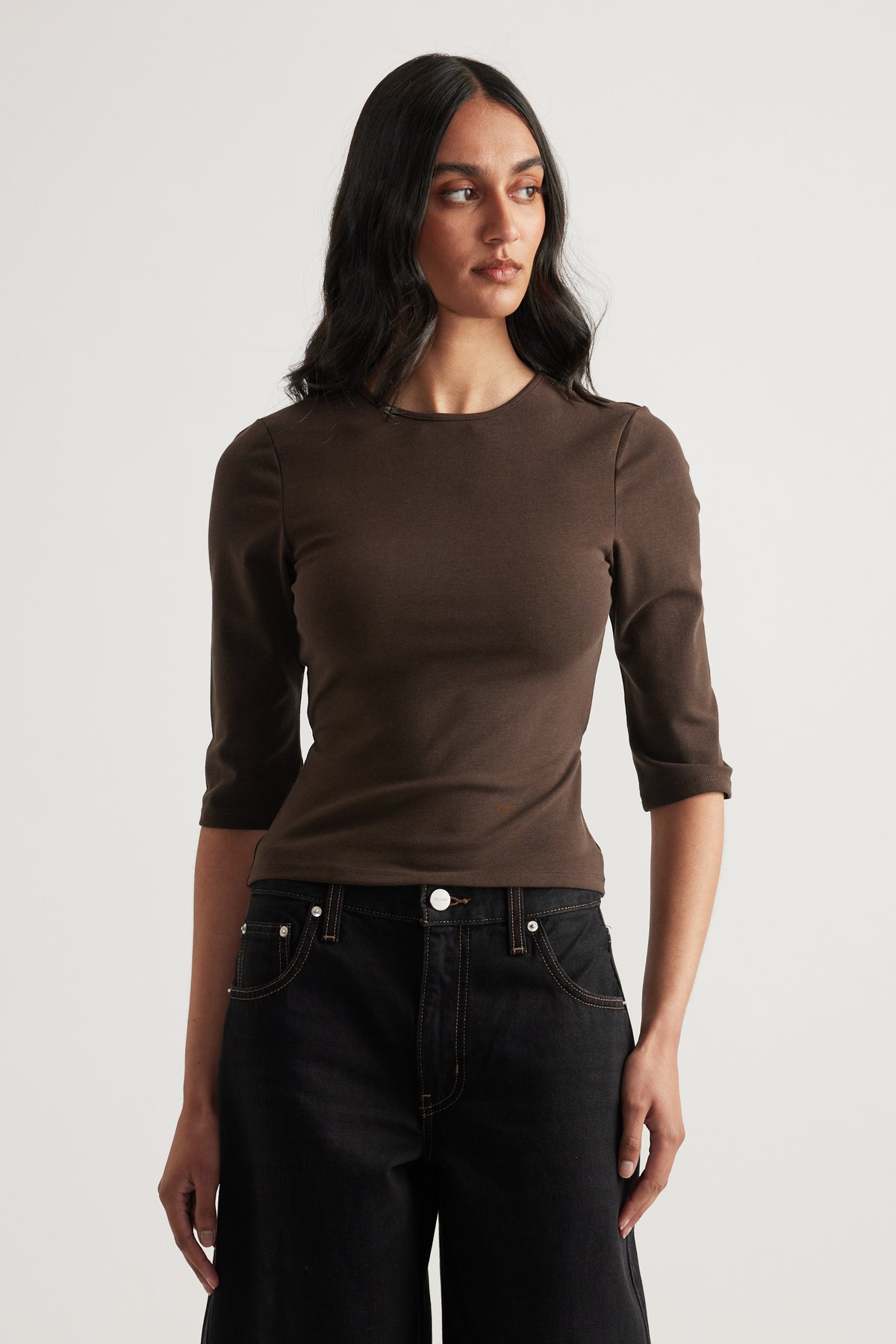 Woman wearing a fitted brown crew neck top with three quarter sleeves and black jeans