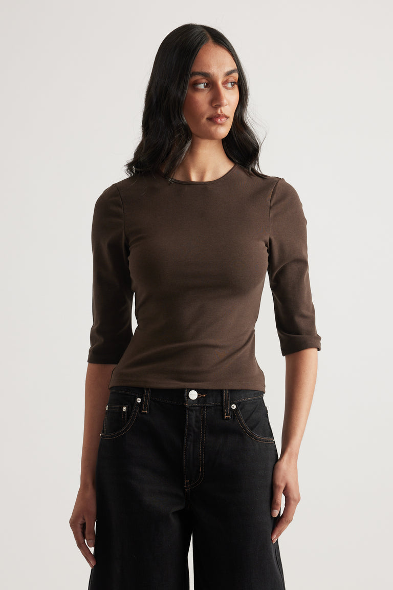 Woman wearing a fitted brown crew neck top with three quarter sleeves and black jeans
