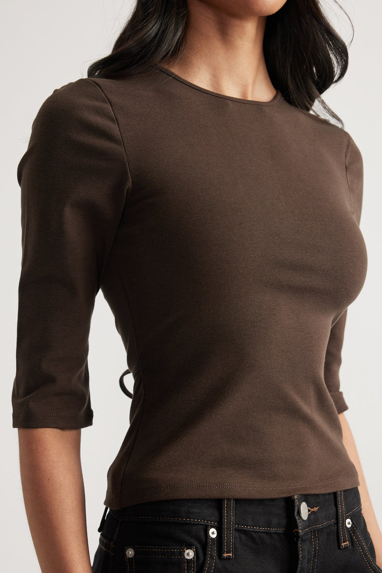 Woman wearing a fitted brown crew neck top with three-quarter sleeves and black jeans