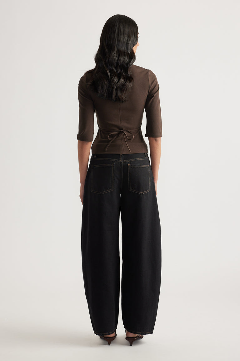 Back view of woman wearing a brown fitted three quarter sleeve top with tie waist and black wide leg jeans