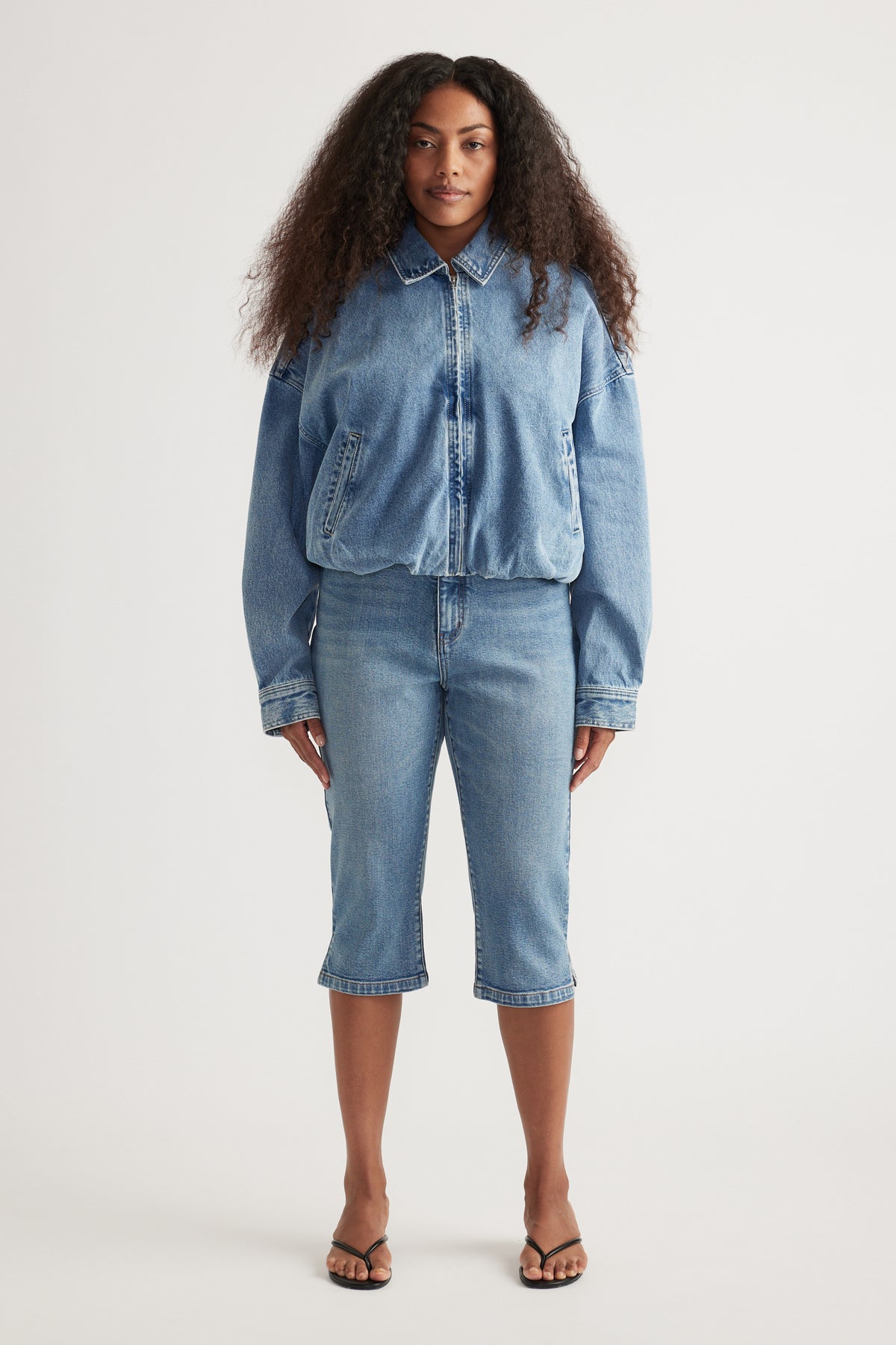 Model wearing a light wash denim bomber jacket with matching cropped jeans and flat sandals