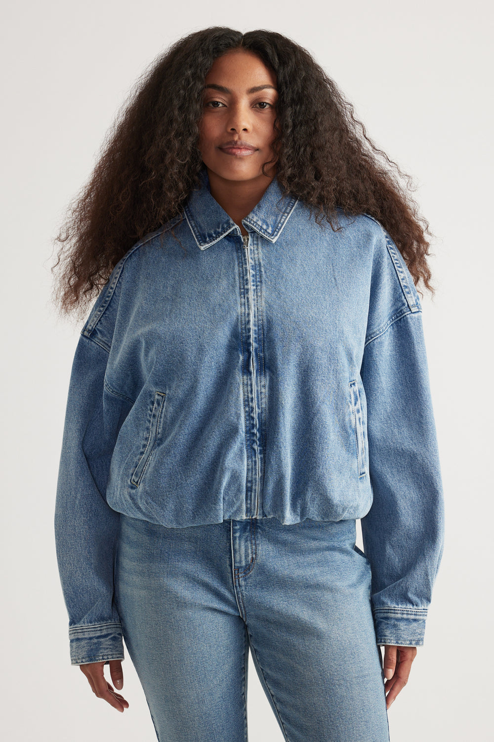 Woman in a light wash denim bomber jacket with a collared zip front, styled with matching jeans