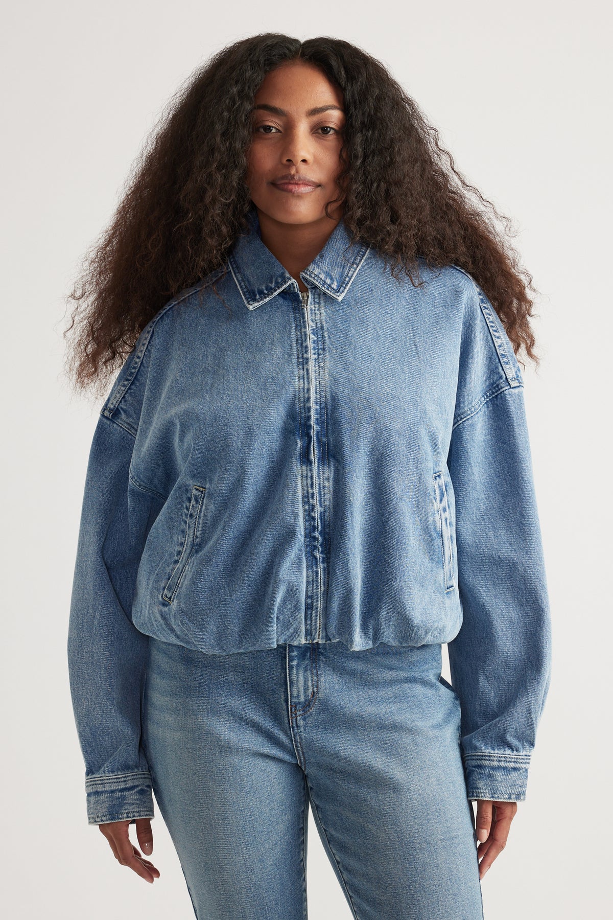 Woman in a light wash denim bomber jacket with a collared zip front, styled with matching jeans