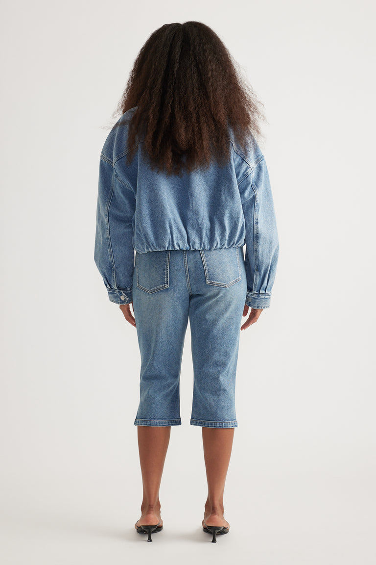 Back view of a woman wearing a light wash denim bomber jacket with matching cropped jeans and heels