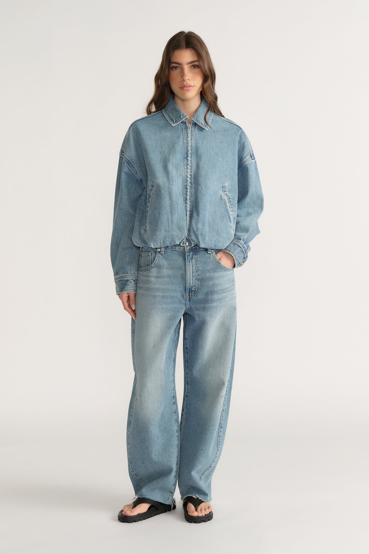 Woman wearing a light wash denim bomber jacket with matching wide-leg jeans and black sandals
