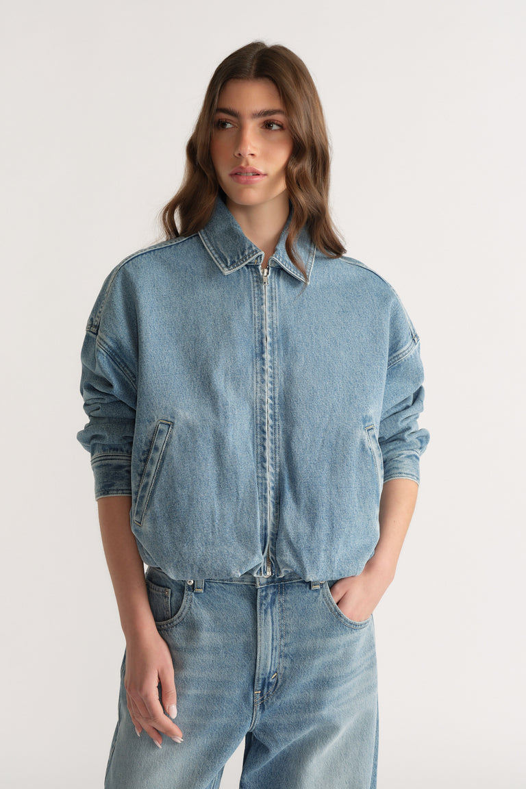 Woman wearing a light wash denim bomber jacket with a zip front and matching jeans