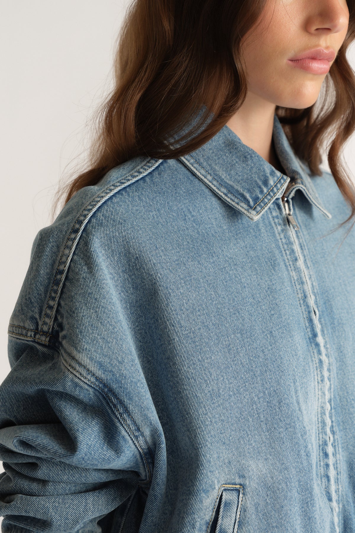 Woman wearing a light wash denim bomber jacket with a collared zip front and angled pocket