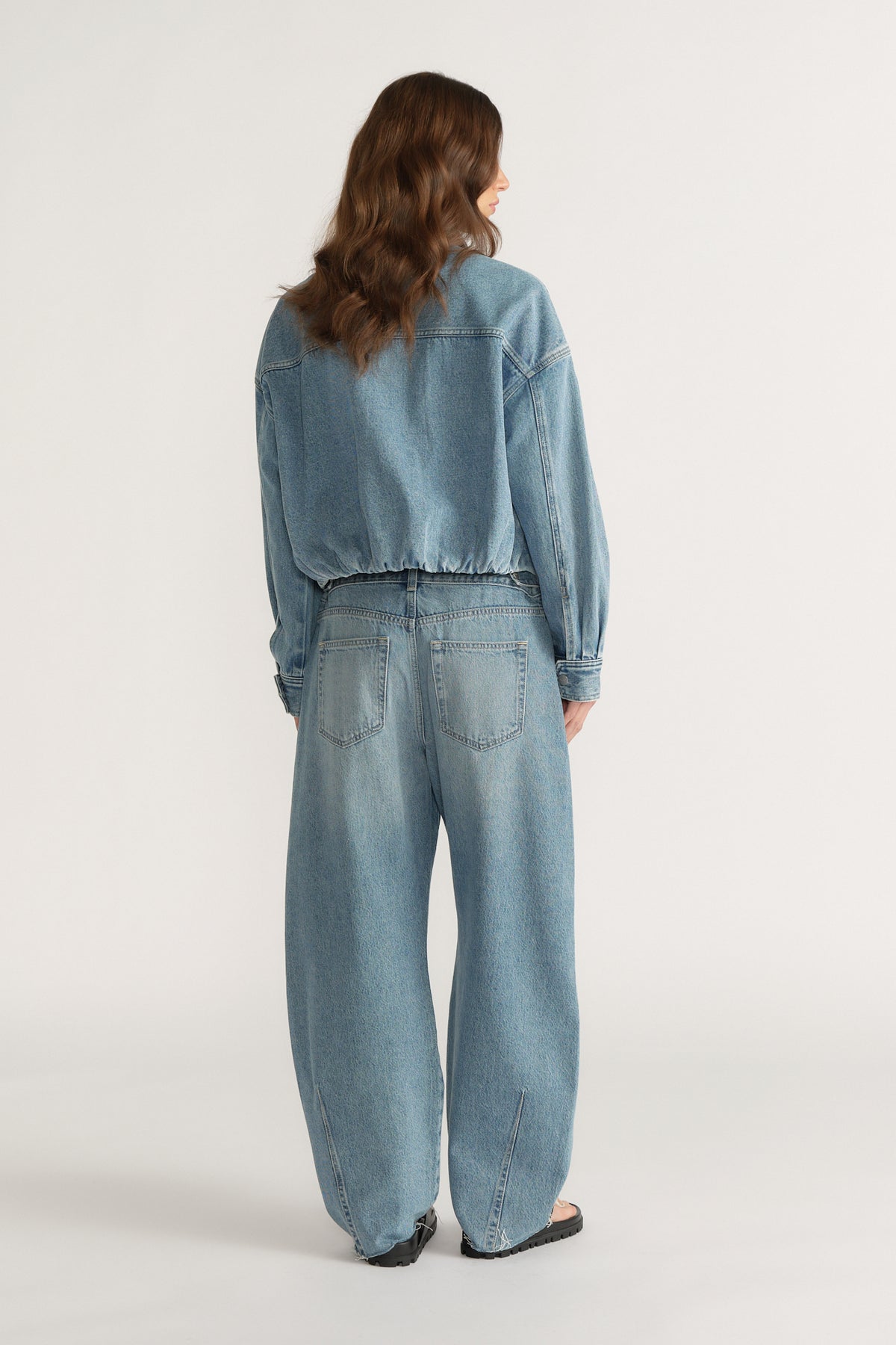 Back view of woman wearing a blue denim bomber jacket with wide-leg jeans