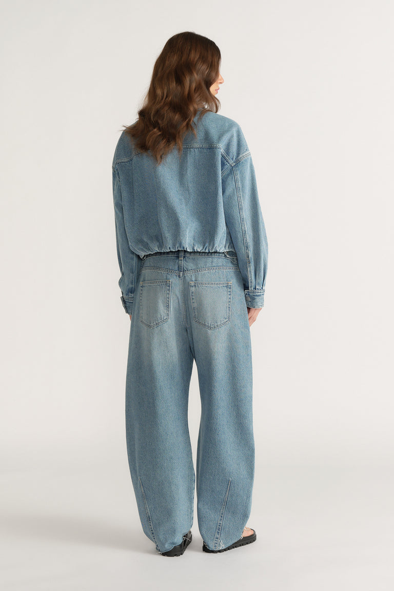 Back view of woman wearing a blue denim bomber jacket with wide-leg jeans