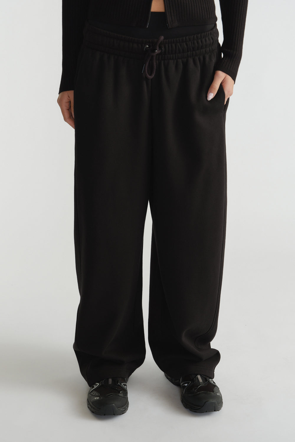 Wide-leg black track pants with elasticated waistband and drawstring, styled with black sneakers and a cropped top
