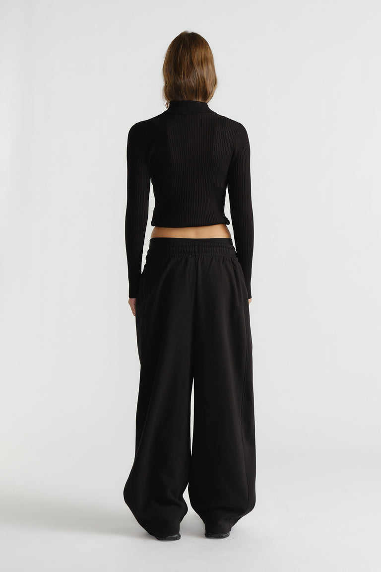 Rear view of a woman wearing relaxed black barrel-shaped track pants paired with a fitted ribbed long-sleeve top