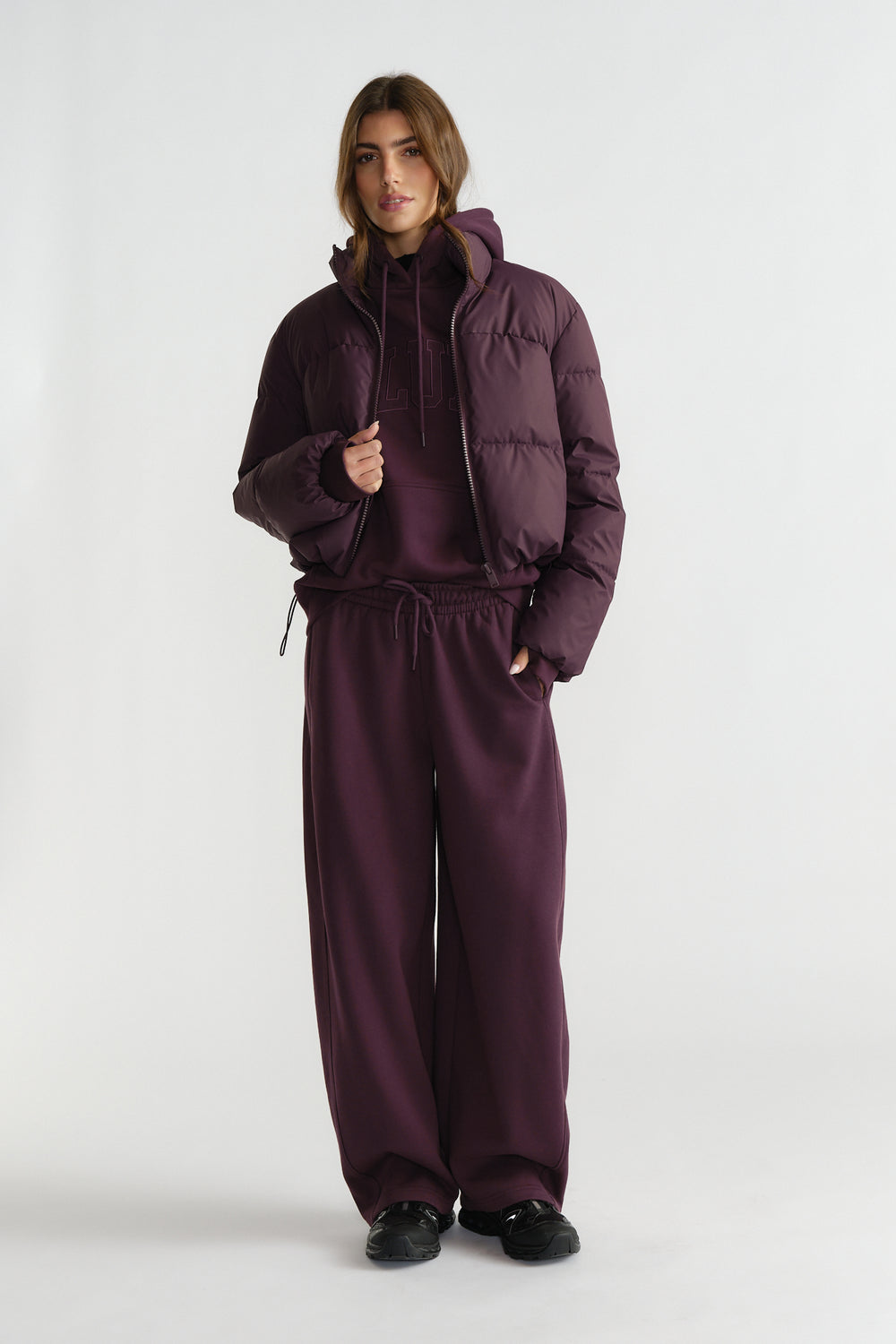 Woman in deep cherry puffer jacket layered over matching hoodie and wide-leg track pants with black sneakers