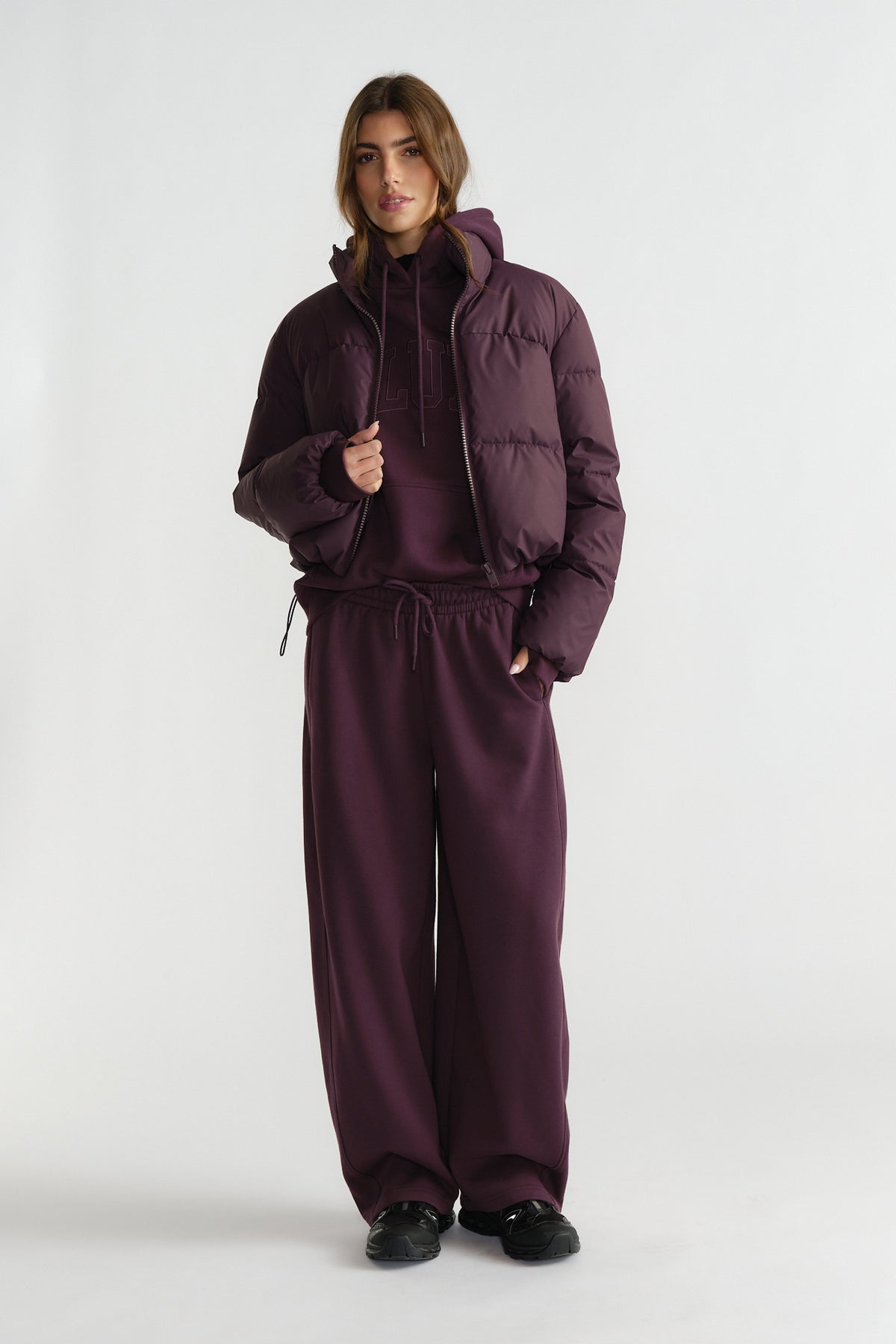 Woman in deep cherry puffer jacket layered over matching hoodie and wide-leg track pants with black sneakers