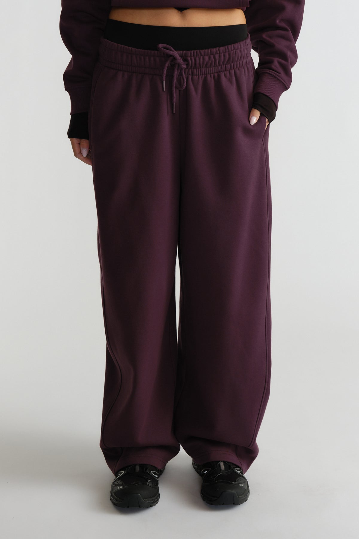 Relaxed-fit deep plum track pants with elastic waistband and drawstring, styled with black sneakers and cropped top