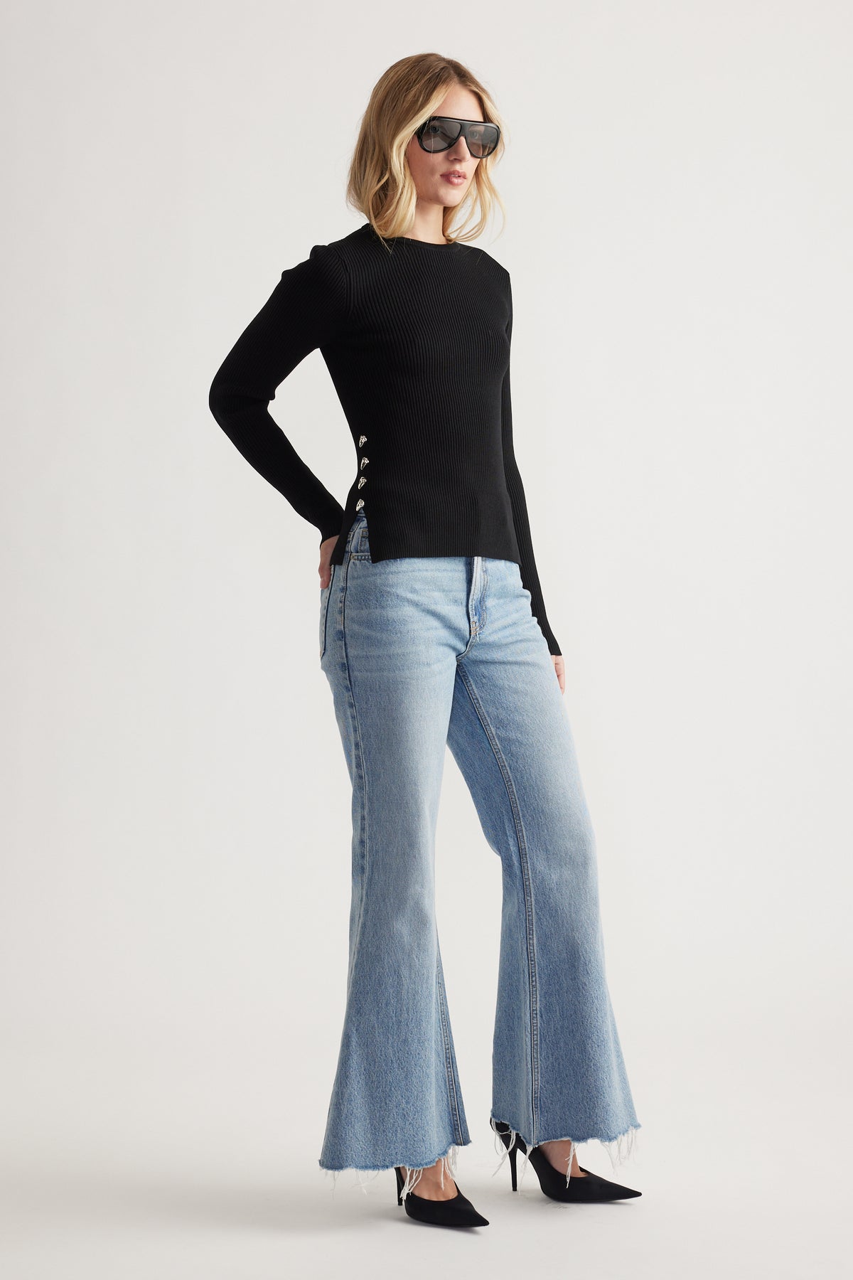 Woman wearing a fitted black long sleeve top with metal side details paired with light flared denim jeans and pointed heels