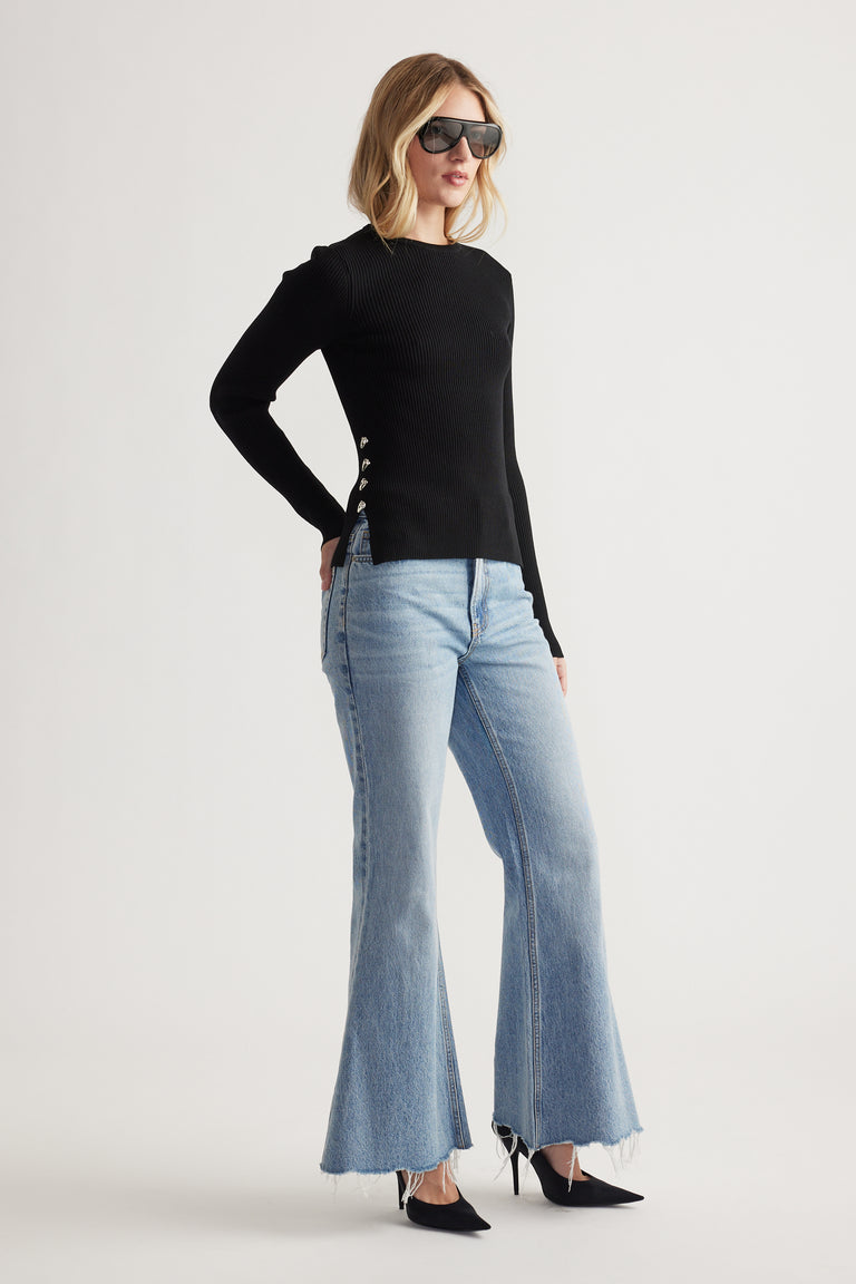 Woman wearing a fitted black long sleeve top with metal side details paired with light flared denim jeans and pointed heels