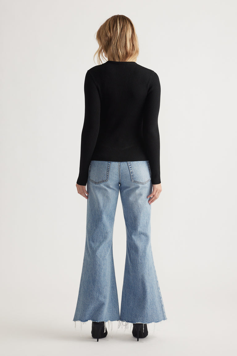 Woman wearing a fitted black long sleeve top paired with high-waisted, light wash wide-leg jeans with frayed hems.