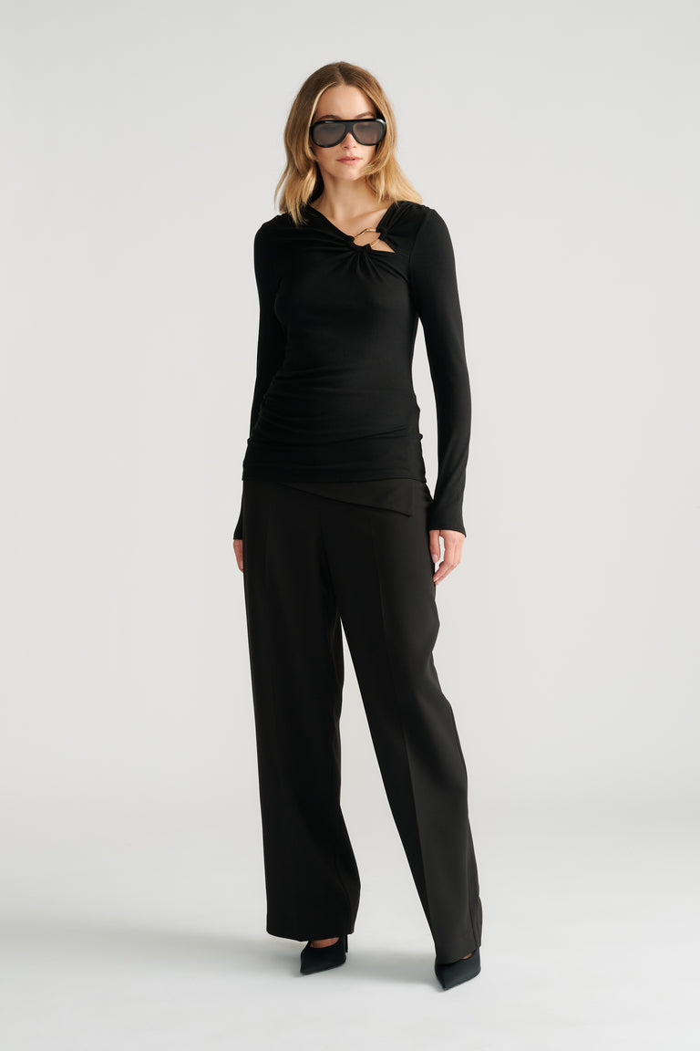 Woman wearing a black long-sleeve top with metal detail paired with wide-leg black pants and black heels.