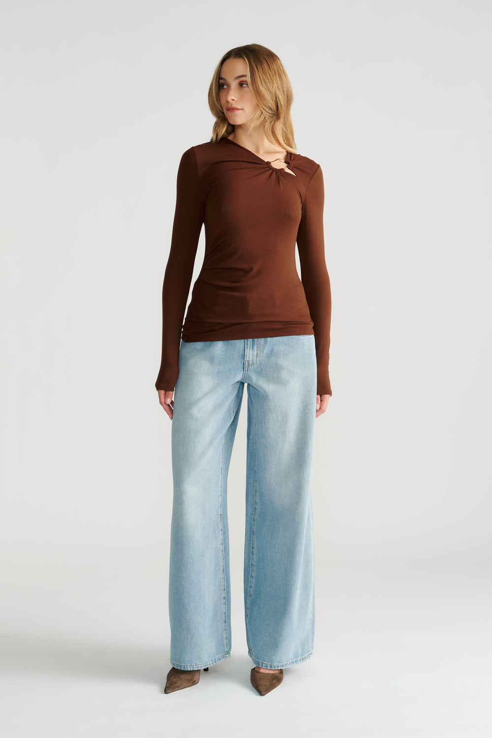Woman wearing a fitted long-sleeve brown top with metal detail and wide-leg light wash denim jeans styled casually.