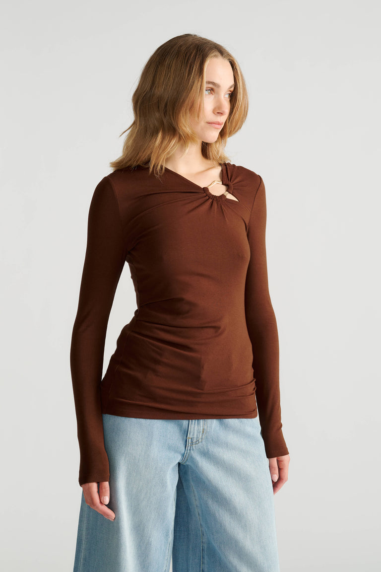 Woman wearing a fitted long-sleeve brown top with metal detail at neckline and light blue wide-leg jeans