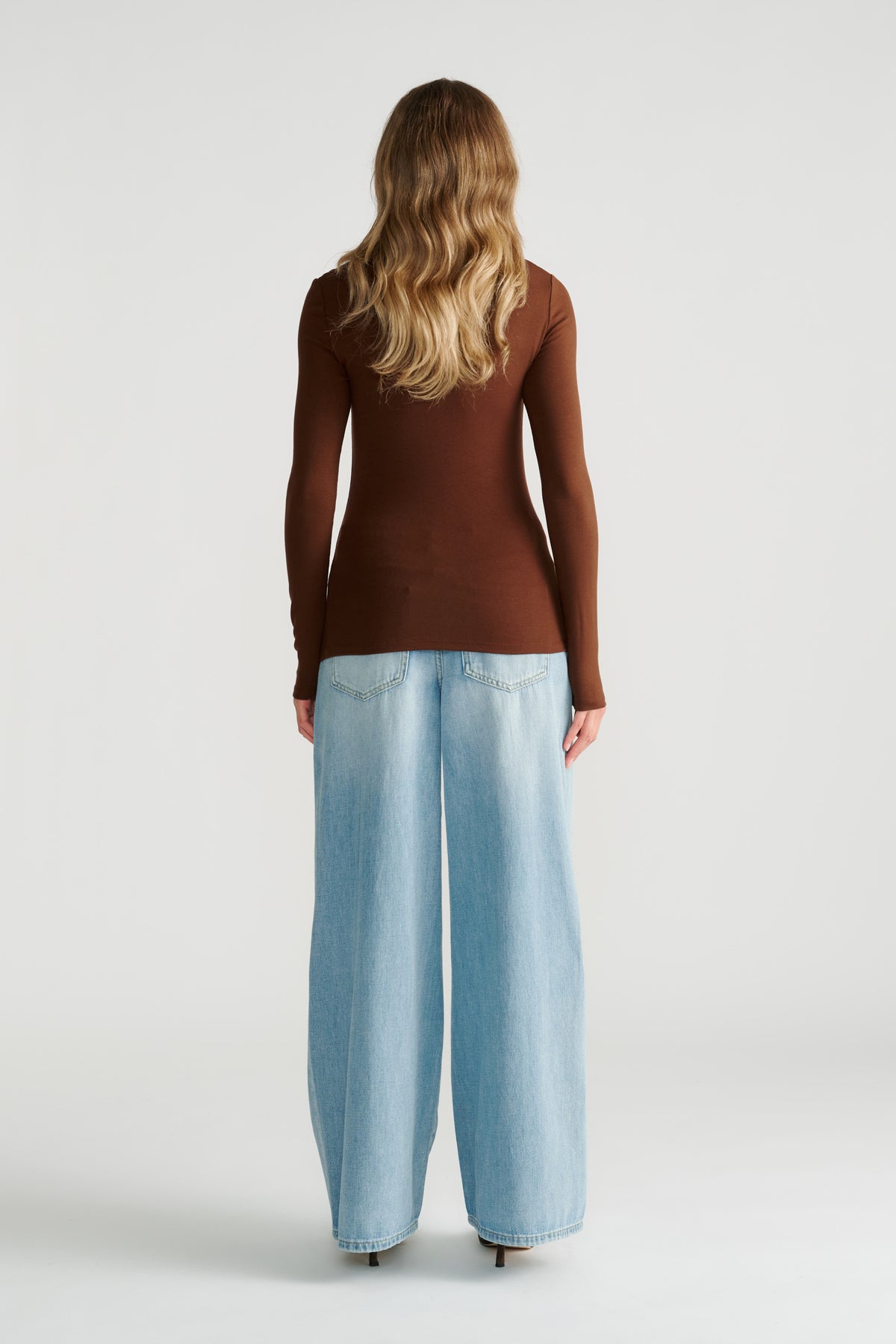Woman wearing a fitted long-sleeve brown top paired with light wide-leg denim jeans, shown from the back.