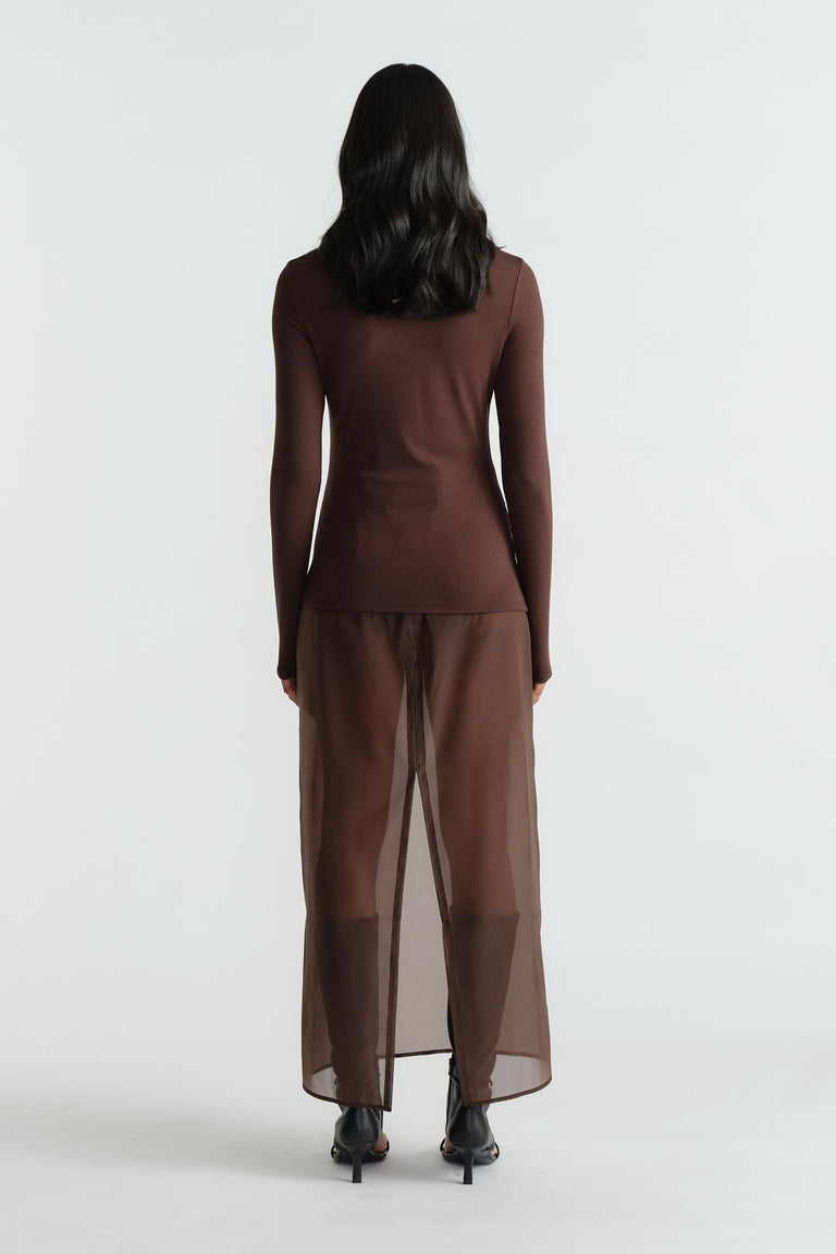 Back view of a woman wearing a rich mocha long-sleeve top paired with sheer brown wide-leg pants and black heels.