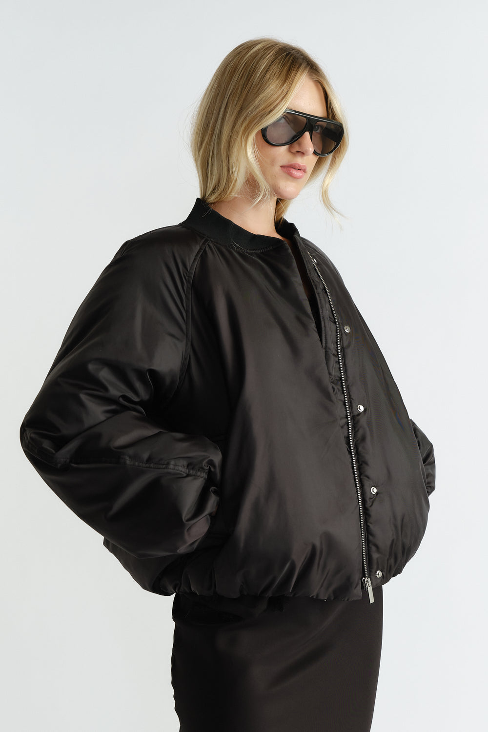 Side view of woman wearing a black oversized bomber jacket with a zip and snap closures paired with a fitted skirt