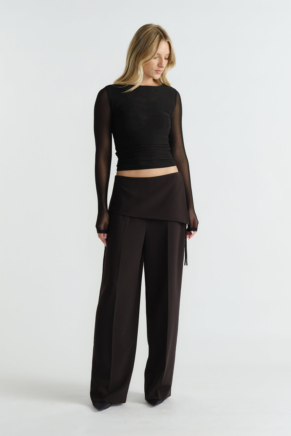 Woman wearing a fitted black mesh long-sleeve top paired with high-waisted wide-leg black trousers and an overlay skirt panel.