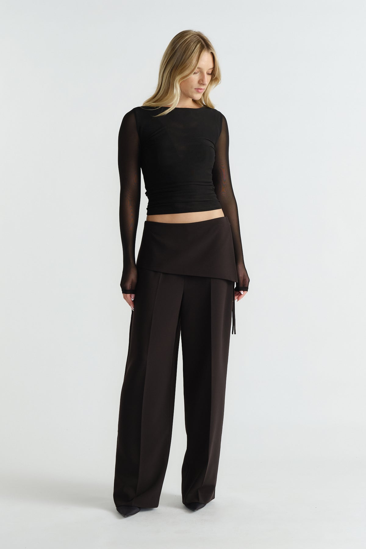 Woman wearing a fitted black mesh long-sleeve top paired with high-waisted wide-leg black trousers and an overlay skirt panel.