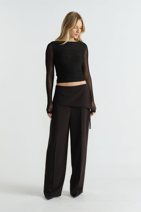 Woman wearing a fitted black mesh long-sleeve top paired with high-waisted wide-leg black trousers and an overlay skirt panel.
