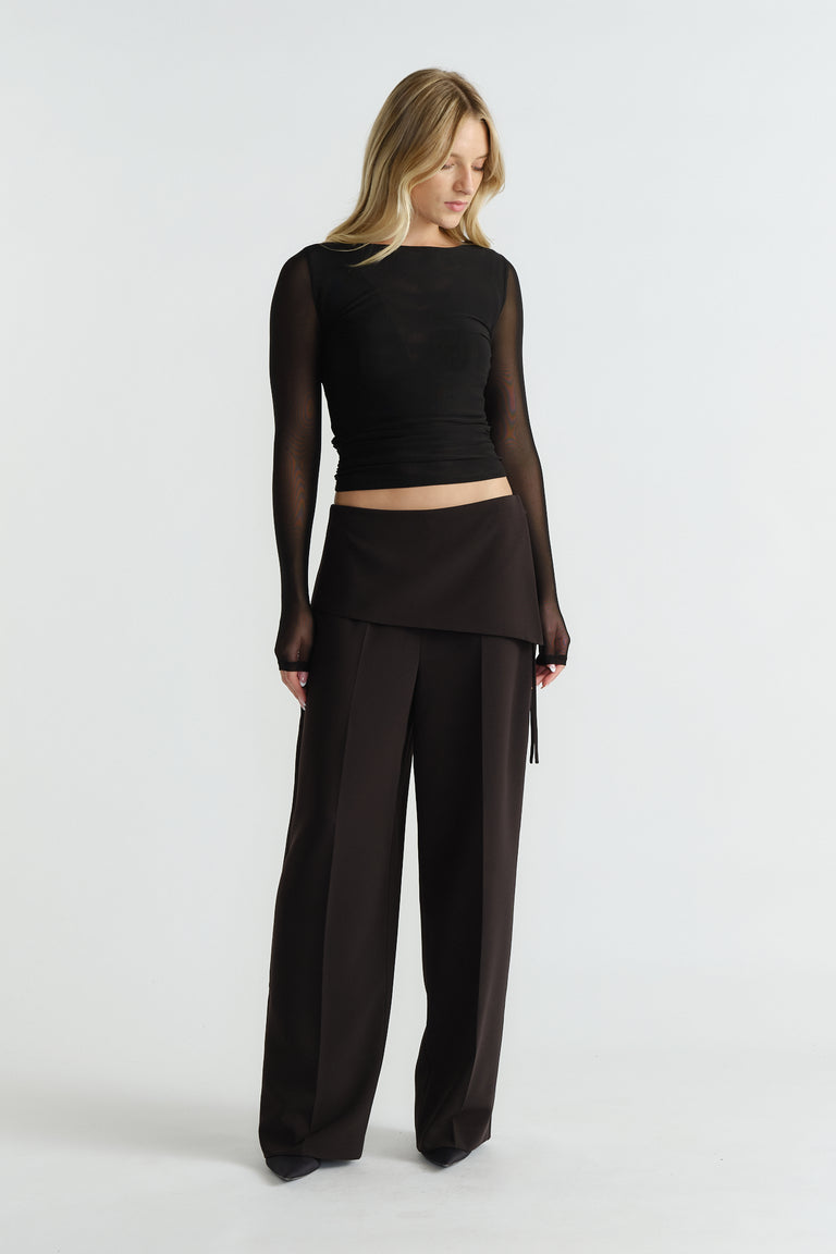 Woman wearing a fitted black mesh long-sleeve top paired with high-waisted wide-leg black trousers and an overlay skirt panel.