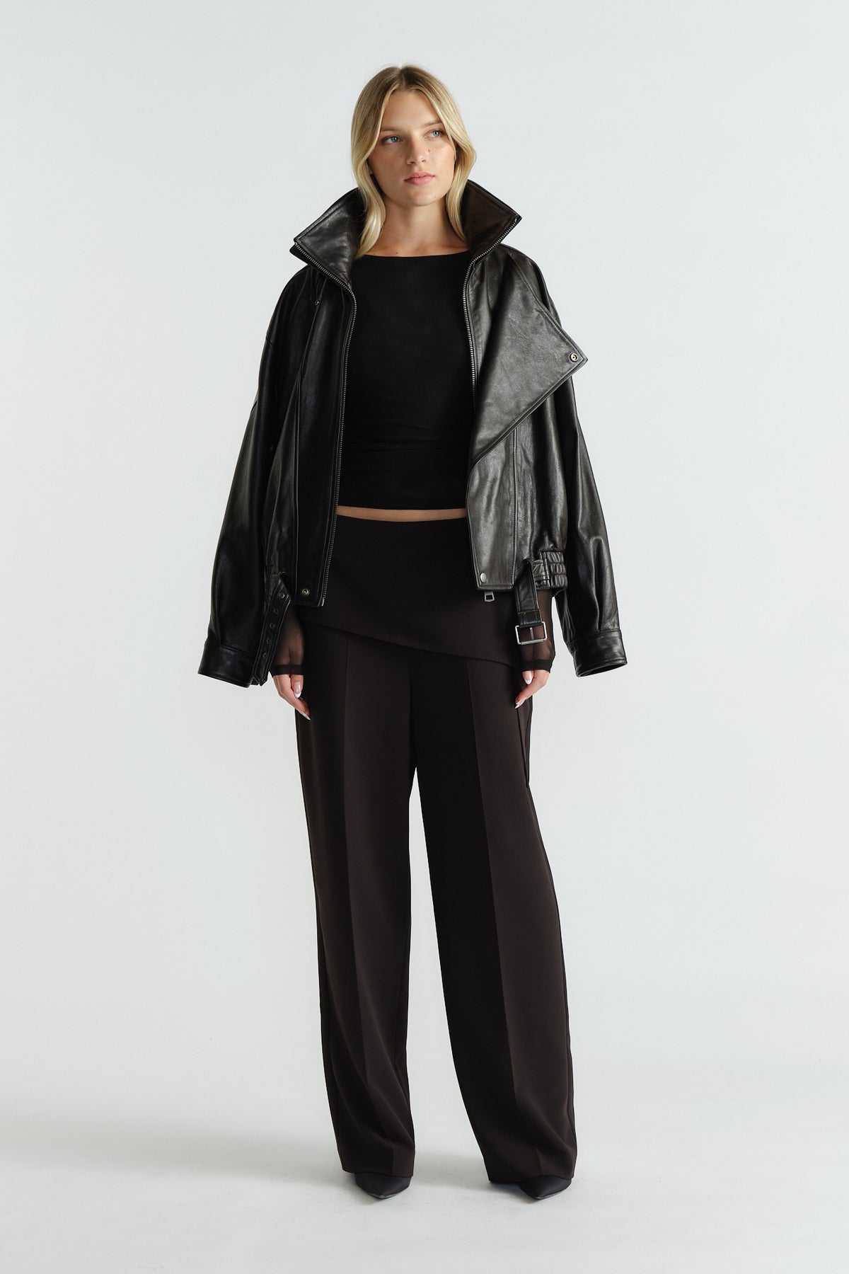 Woman wearing a fitted black mesh top styled with a loose leather jacket and wide-leg dark trousers for an edgy look.