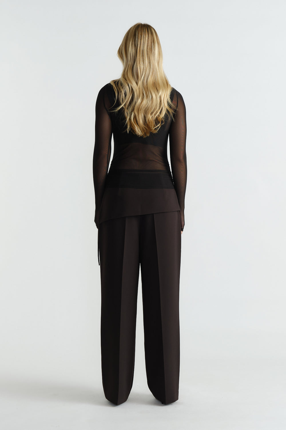 Woman wearing a sheer black mesh top paired with high-waisted wide-leg black trousers, back view.