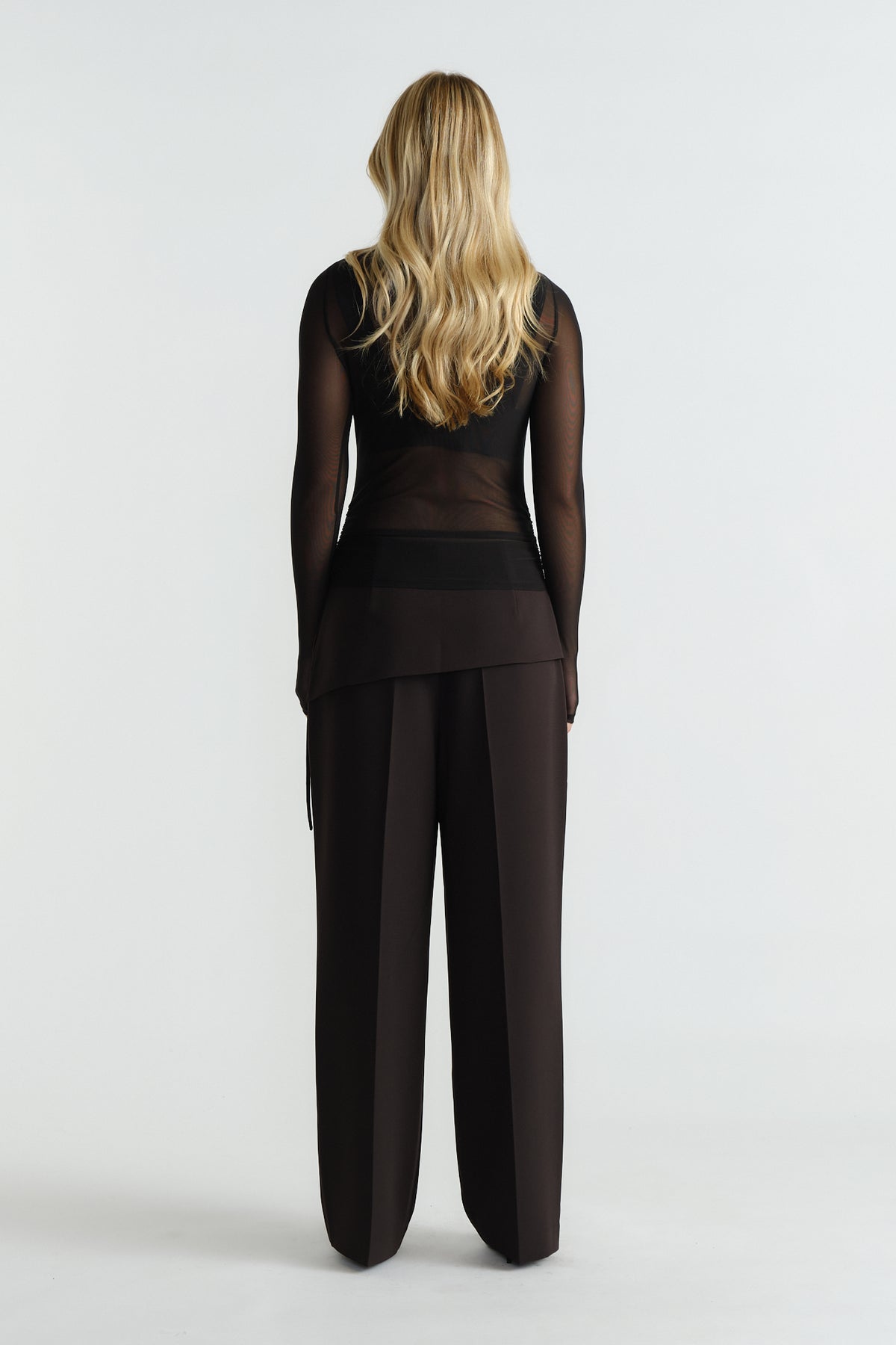 Woman wearing a sheer black mesh top paired with high-waisted wide-leg black trousers, back view.