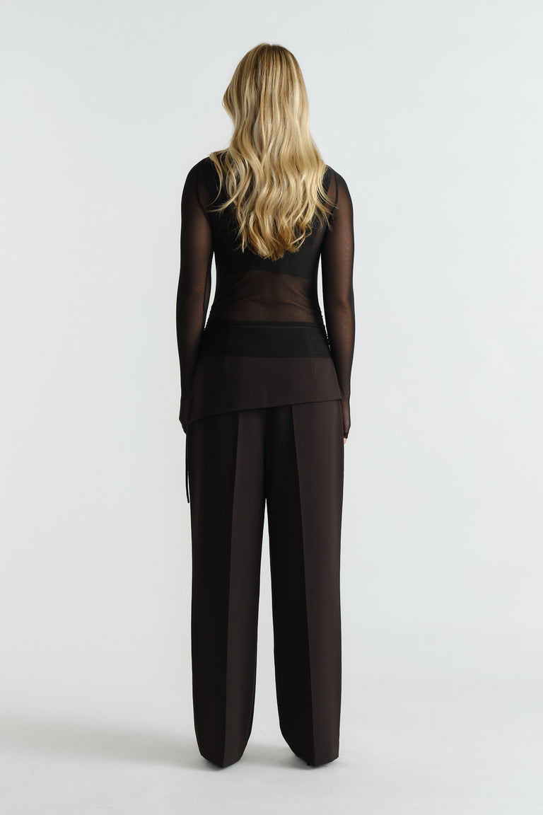 Woman wearing a sheer black mesh top paired with high-waisted wide-leg black trousers, back view.