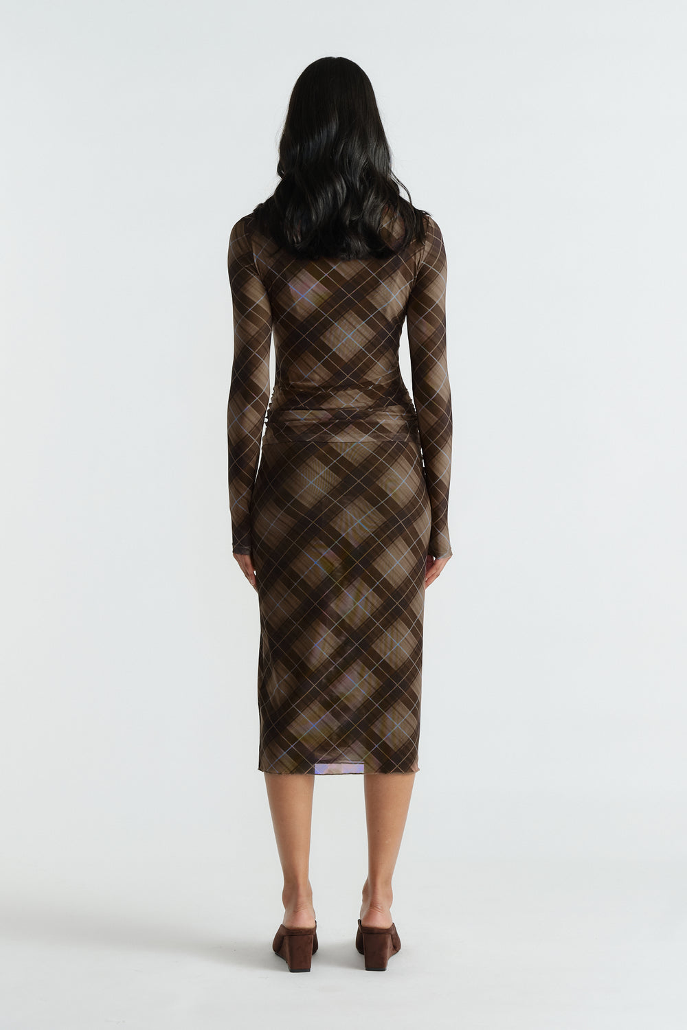 Rear view of woman wearing a fitted brown checked mesh top and matching midi skirt with long sleeves and block heels.