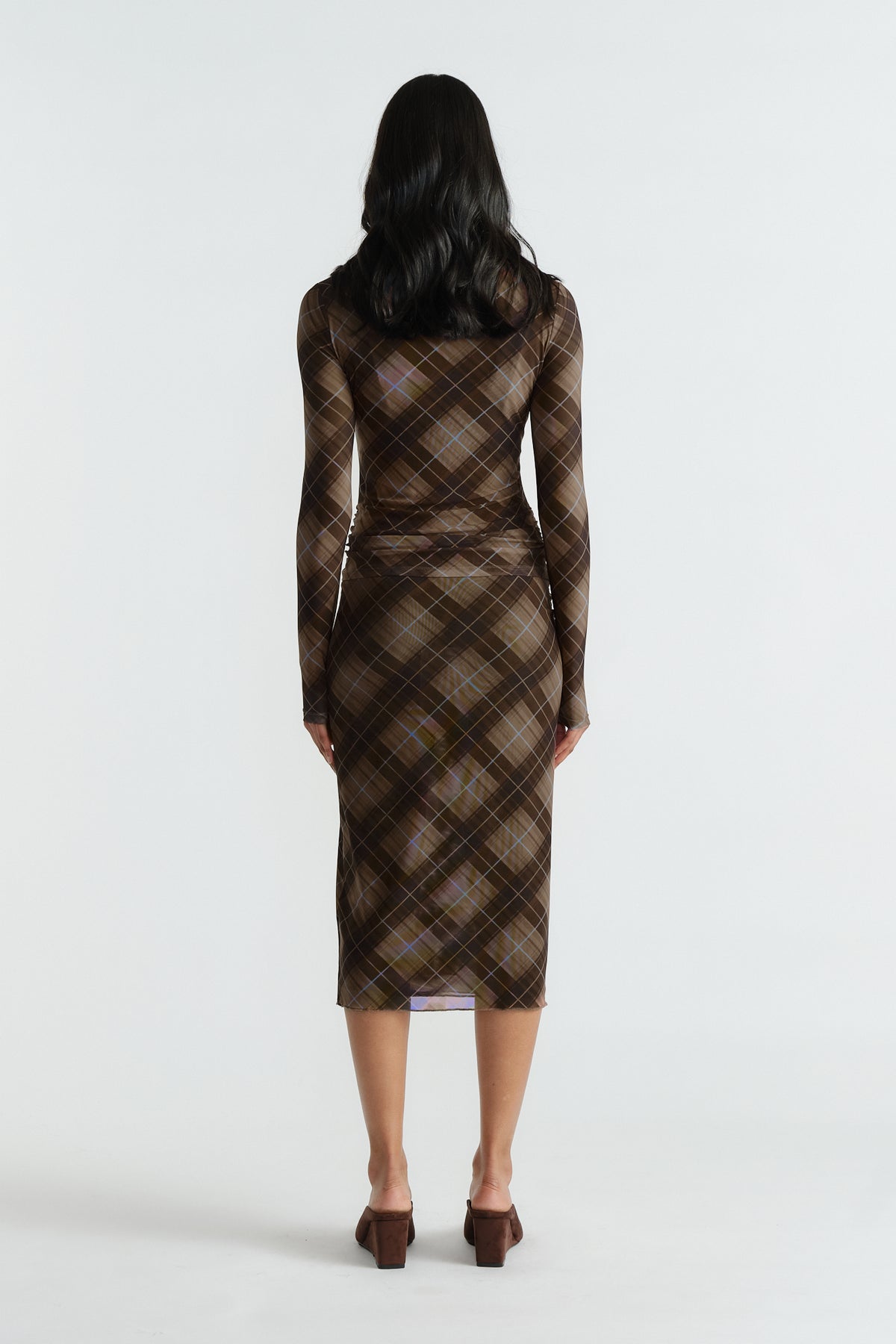 Rear view of woman wearing a fitted brown checked mesh top and matching midi skirt with long sleeves and block heels.
