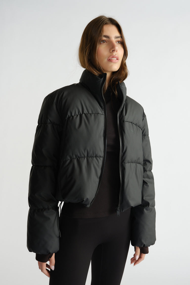 Woman wearing a black cropped puffer jacket with high collar over fitted black leggings and a dark top