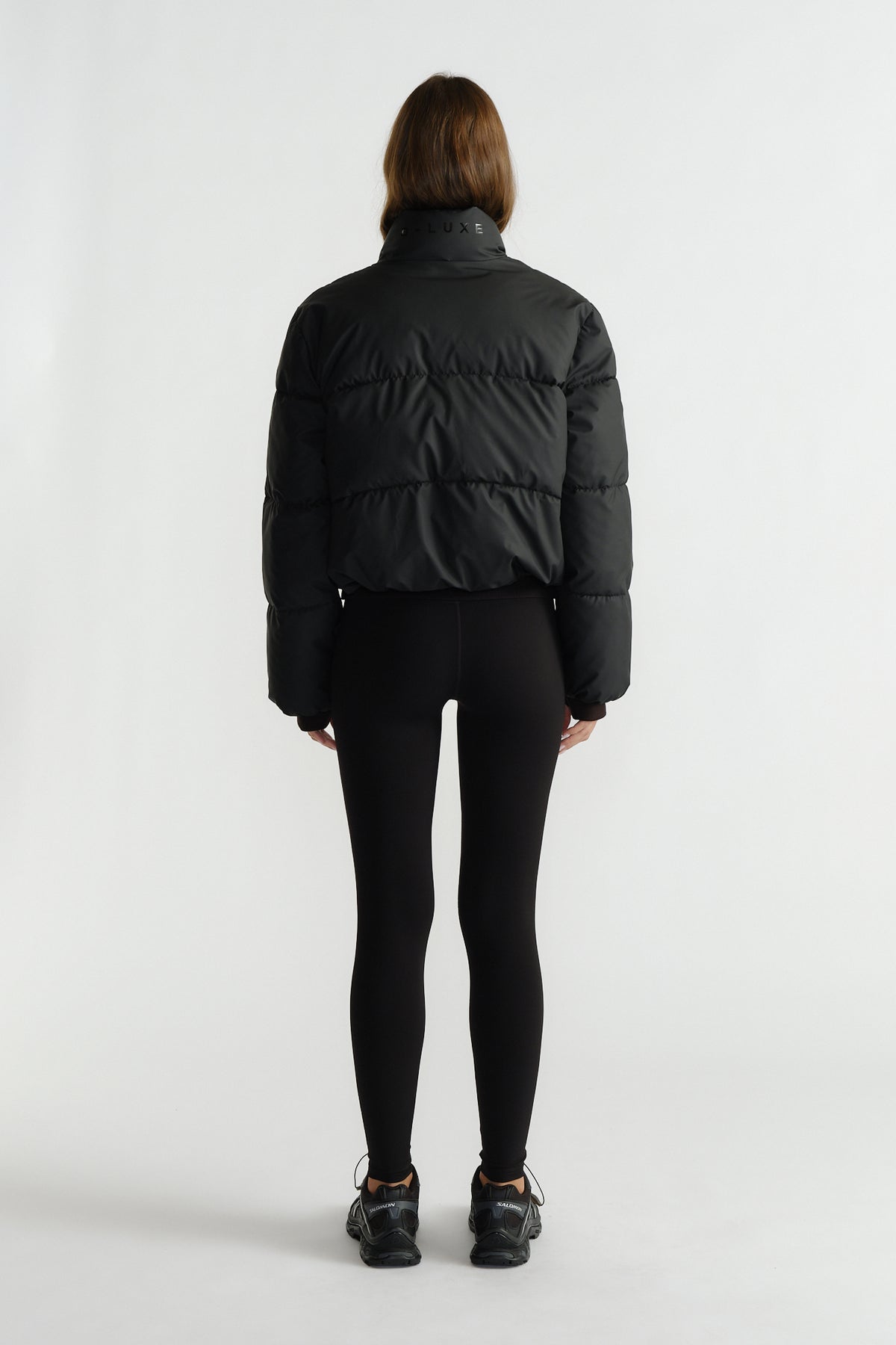 Back view of a woman wearing a black cropped puffer jacket styled with fitted black leggings and sneakers