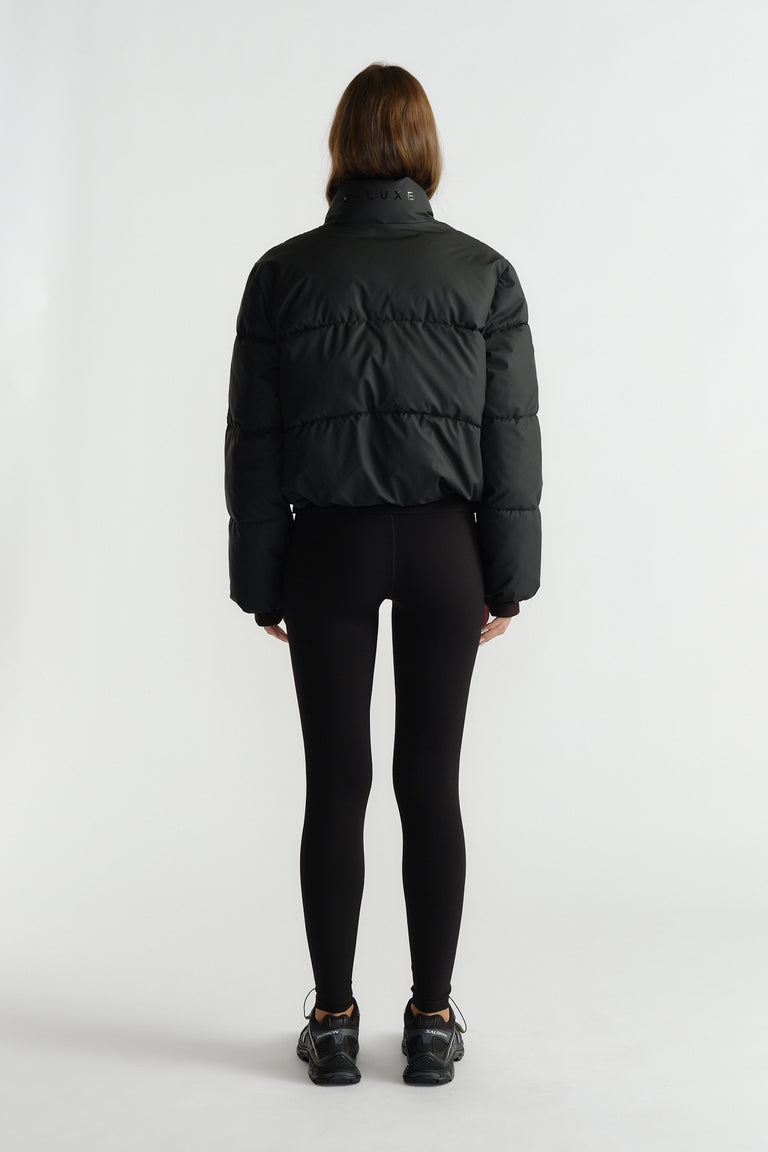 Back view of a woman wearing a black cropped puffer jacket styled with fitted black leggings and sneakers