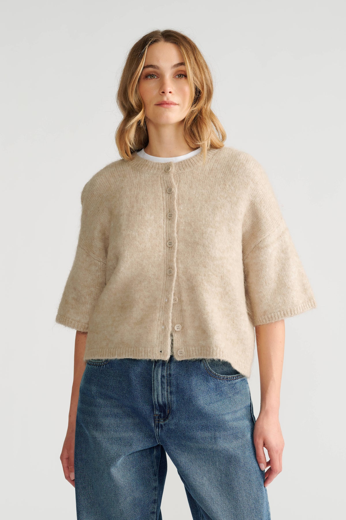 Woman wearing a soft beige boxy knit cardigan with short sleeves paired with relaxed fit classic blue jeans