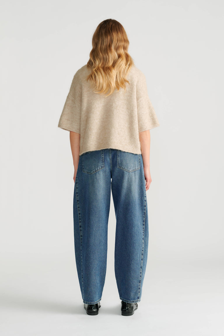Woman wearing a soft beige boxy knit cardigan paired with relaxed-fit blue denim jeans and black shoes, seen from behind.